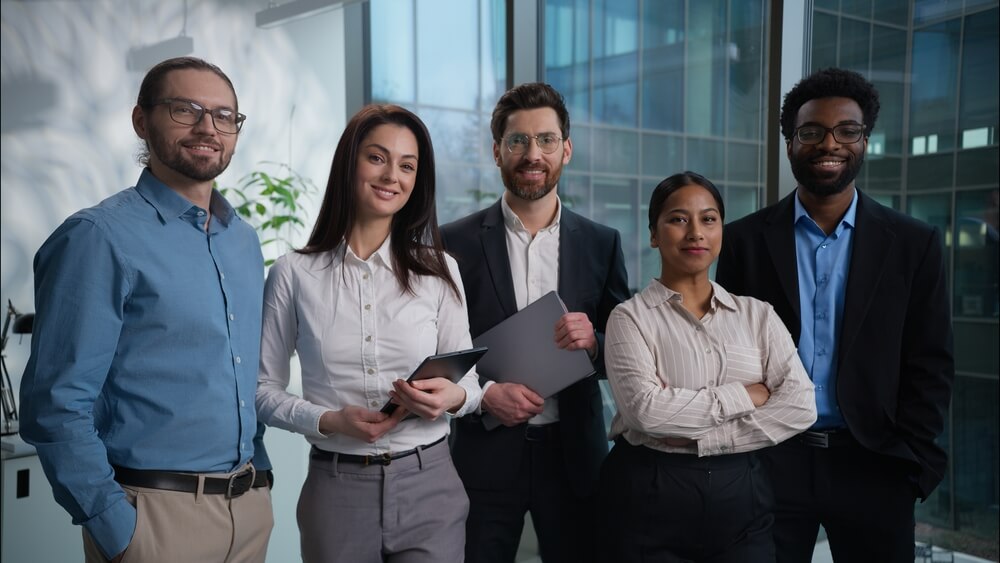 Diverse team of professionals standing together in an office, representing how to communicate mergers and acquisitions to employees clearly.