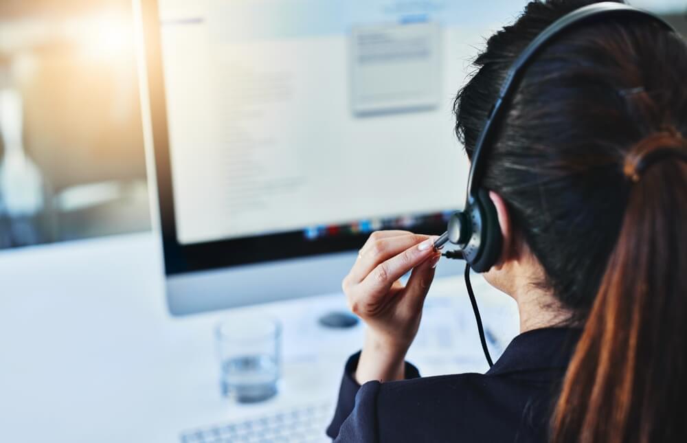 A call center representative wearing a headset and assisting a customer on her computer, showing the versatility of call center services by industry.