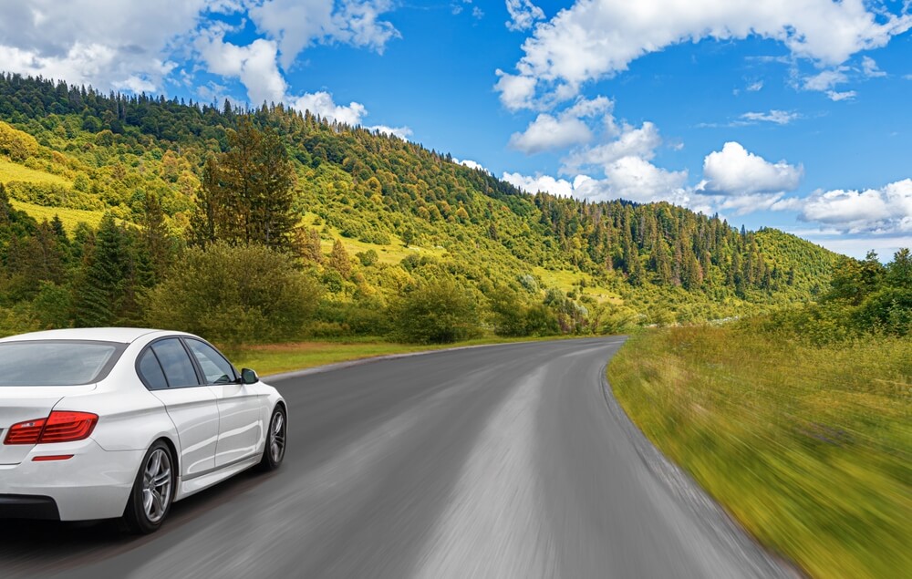 Car driving on an open road through nature, representing peak demand periods across auto insurance busy seasons