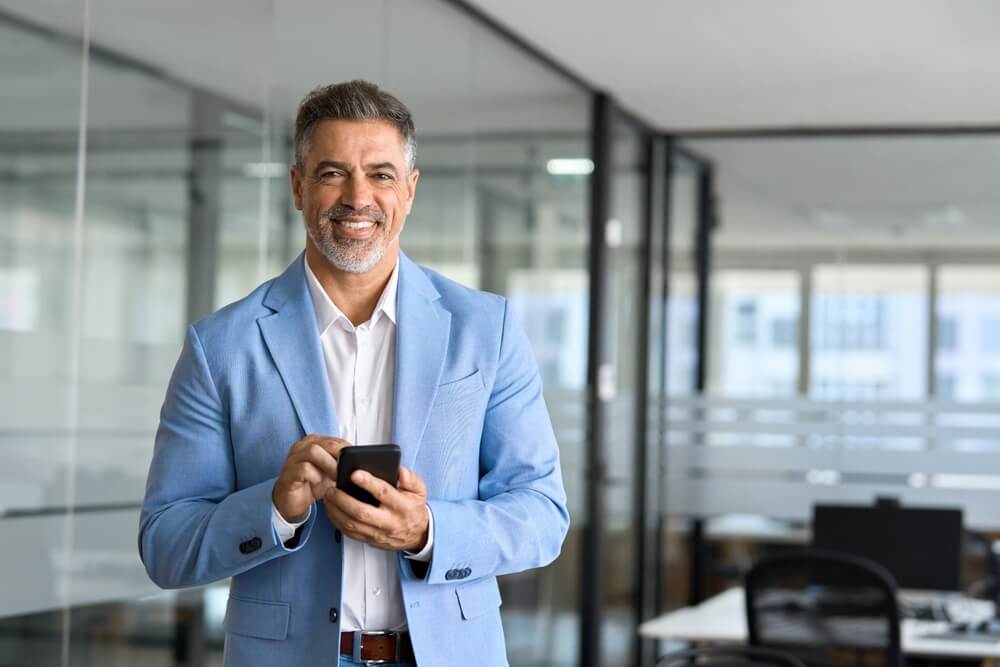 Smiling franchise owner checks his phone in a modern office while thinking about how do franchise owners get paid?