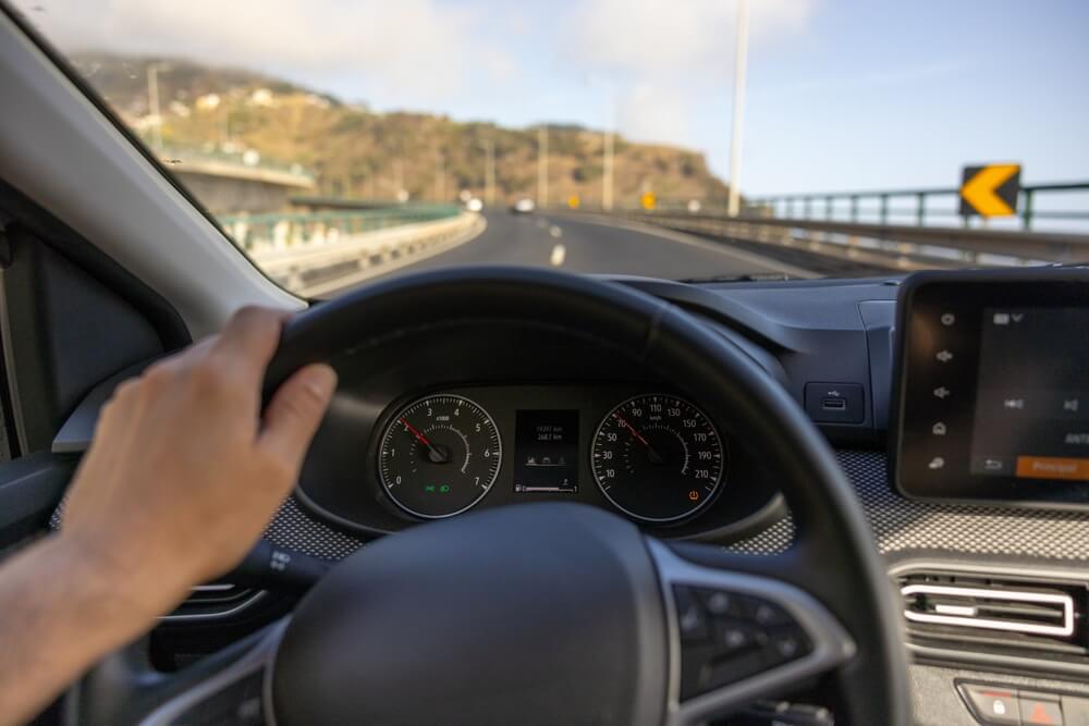 Man seen from hands only on steering wheel with road stretching ahead and mileage counter - concept of telematics on mileage usage.