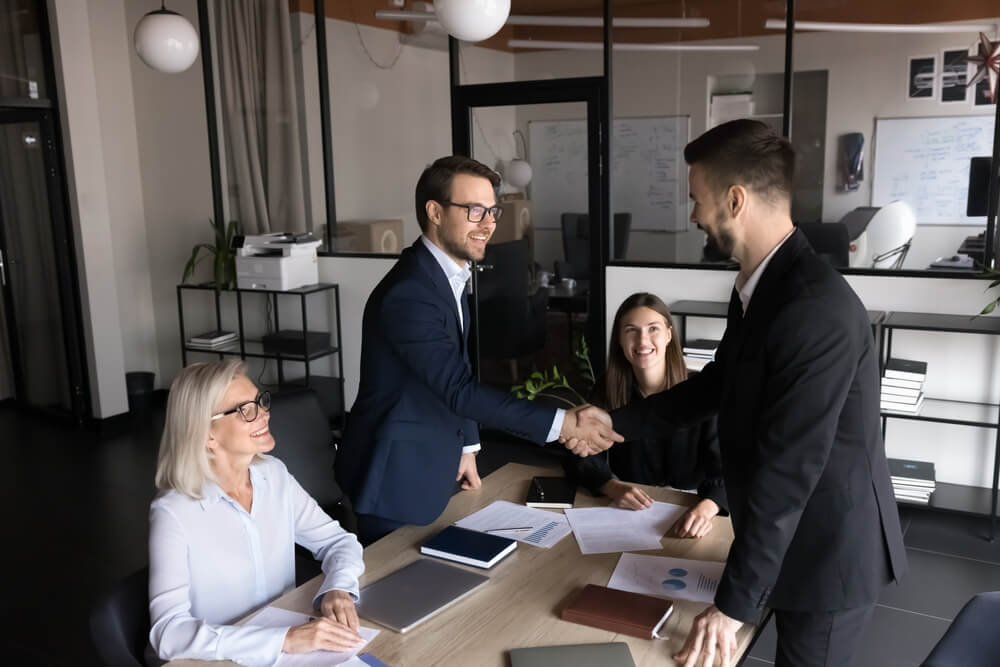 Group of shareholders greeting each other before negotiation in modern conference room, shaking hands, expressing mutual respect, thanking for successful collaboration and future partnership in office.