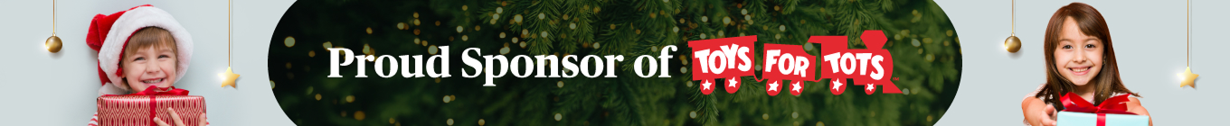 Two smiling children wearing Santa hats hold wrapped gifts on each side of a banner that reads “Proud Sponsor of Toys for Tots” with festive greenery in the background.