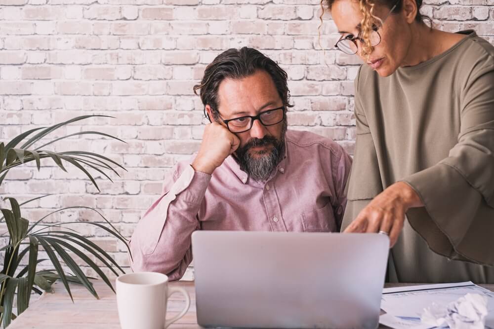 Couple of insurance agency owners talking in front of an open laptop on the desk about when to sell their agency. 