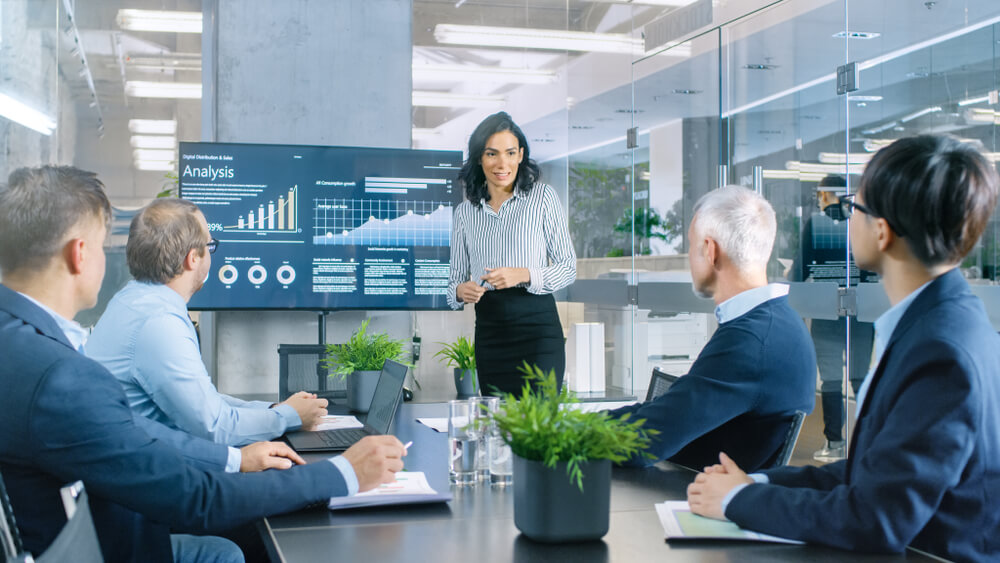 Woman presenting financial analysis to four investors during a meeting about an insurance agency acquisition