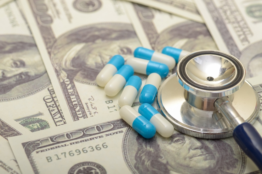 Stethoscope and prescription pills on cash representing rising insurance costs.
