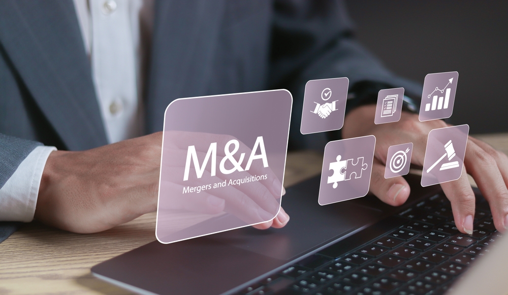 Business professional using a laptop with M&A mergers and acquisitions transaction icons.